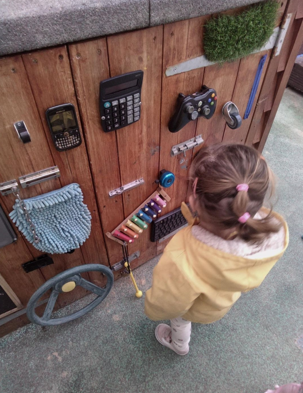 Playing with a busy board wall in Kindergarten Kids Nursery outside play area in Whitstable