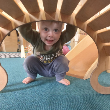 Curious boy peers through wooden tunnel at Whitstable Day Nursery